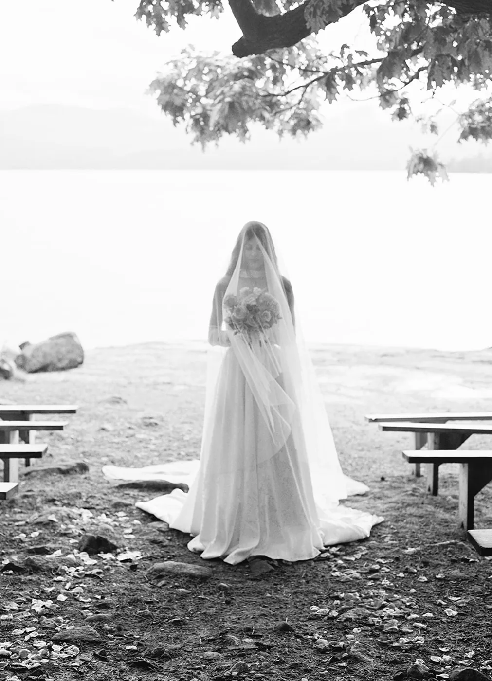 Bride in a veil standing on a lakeshore in black and white
