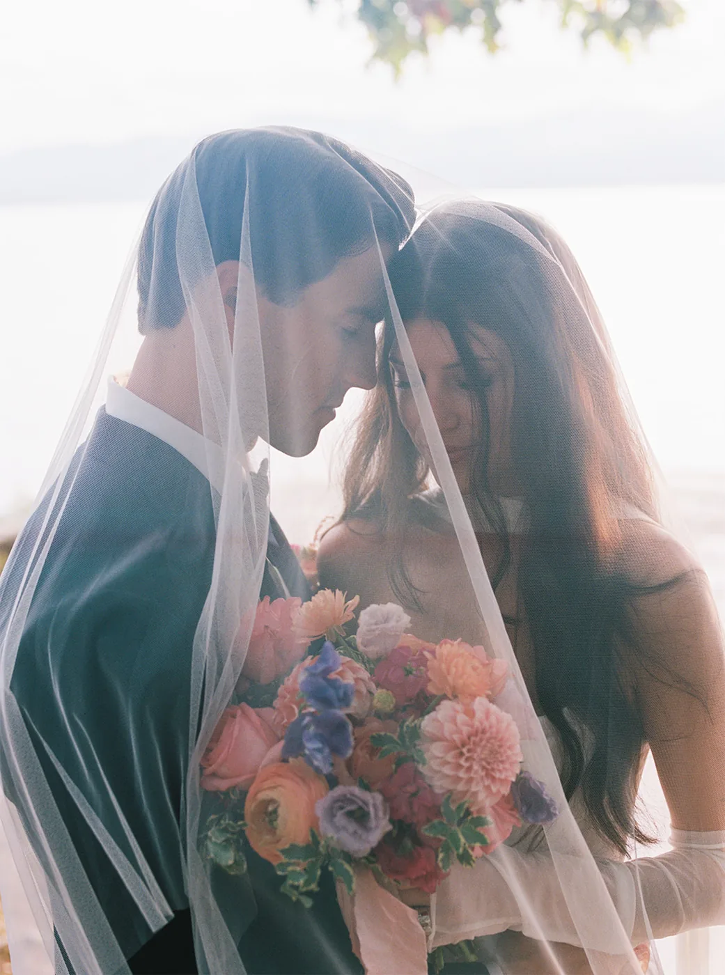 Newlyweds embracing under a veil with a bouquet