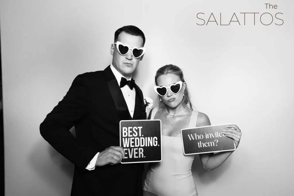 Bride and groom in sunglasses holding signs in a black and white photo booth portrait