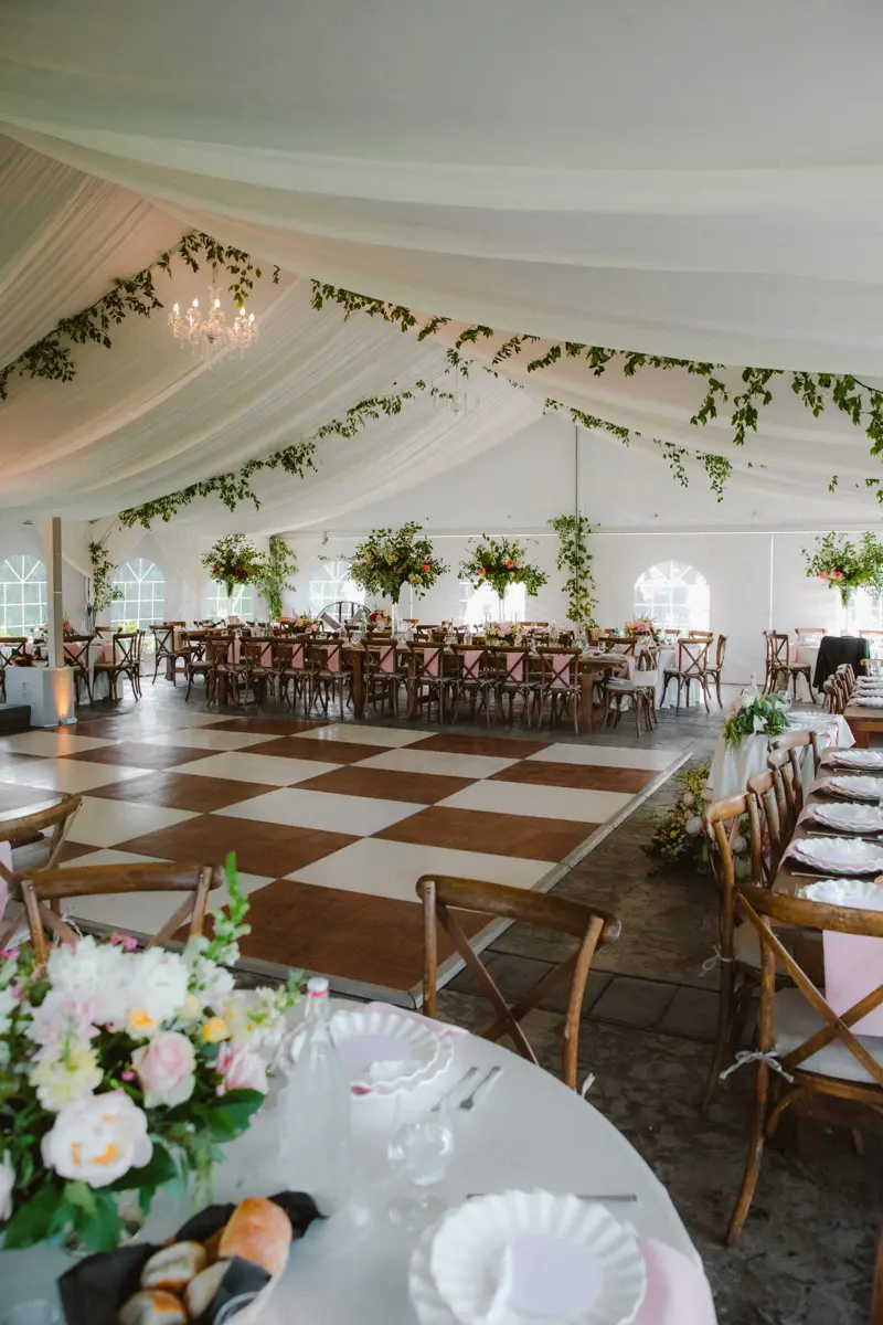 Empty tent reception with dining tables, chandeliers and a checkered dance floor