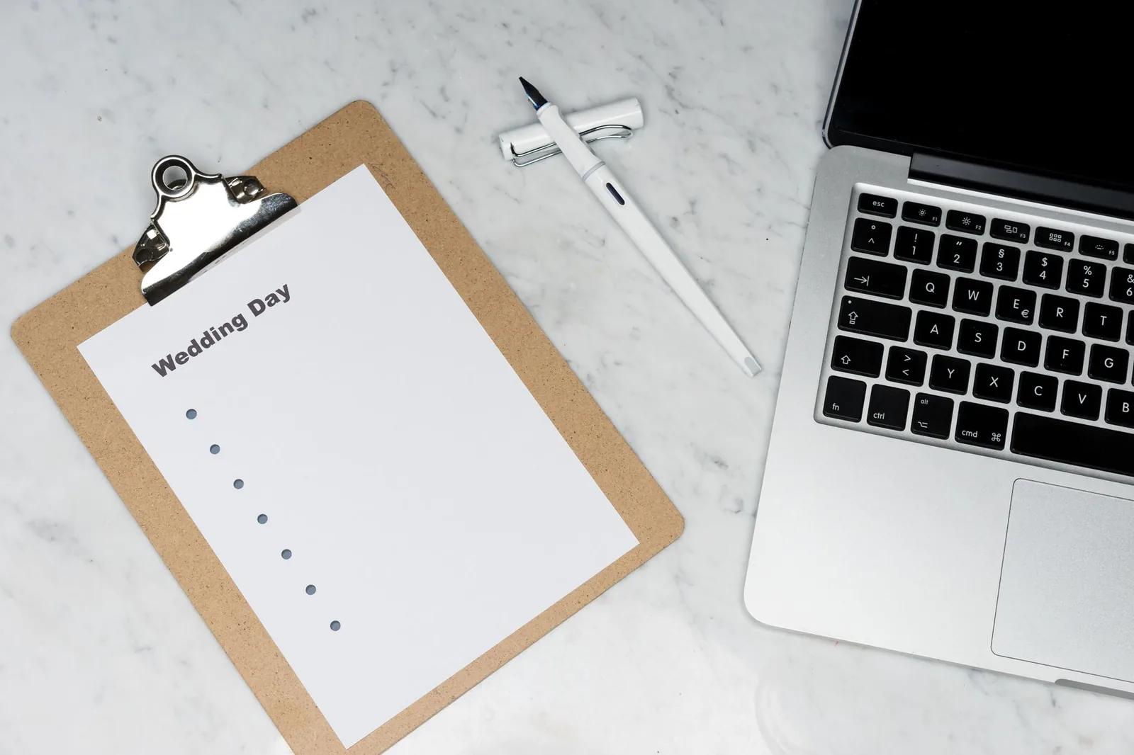Wedding-day planning clipboard beside a laptop and pen