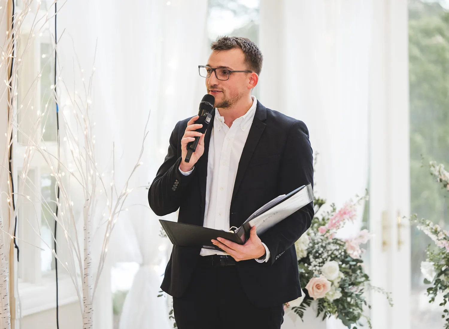 VARA MC holding a microphone and an open folder at a wedding