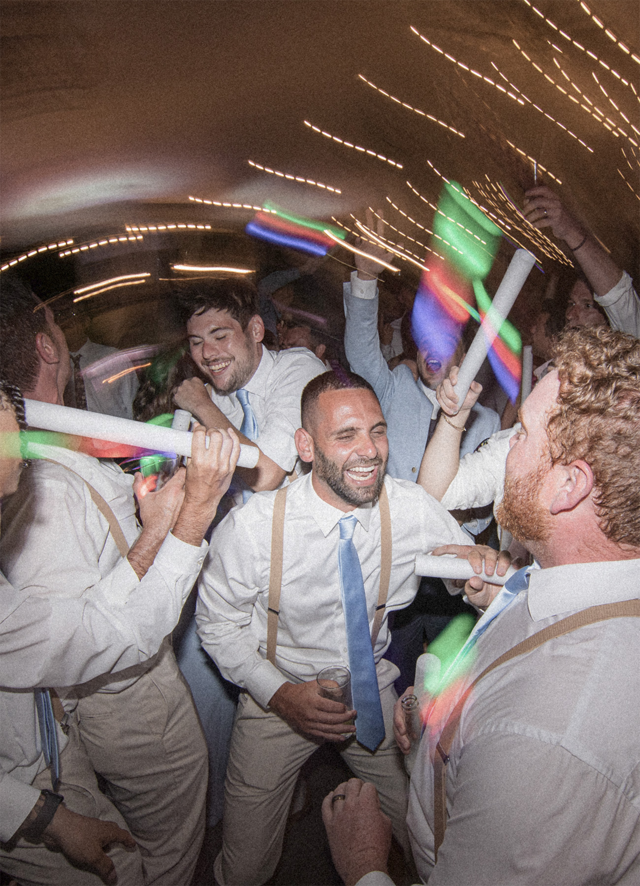 Wedding guests celebrating on a packed dance floor with LED foam sticks during a high-energy reception hosted by VARA DJs.